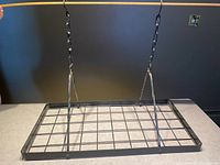 Front view of the rectangular black metal ceiling-mounted pot rack suspended by hanging chains on a countertop.