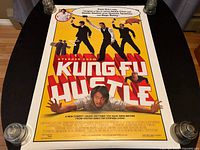 Poster laid flat on black table with weights on corners showing full front face, clear image of title and characters