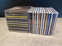 Stacked view of 26 CD jewel cases showing album spines, mostly 1990s-2000s pop and alternative albums.