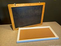 Photo showing vintage chalkboard with solid wood frame and metal hanging hardware, alongside a framed corkboard with white frame.