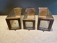 Three antique dry goods bins shown side by side with slanted wood and glass fronts and metal sides and bases.