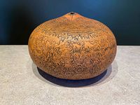 Front view of a round, hand-carved Peruvian mate burilado gourd showing detailed folk art scenes around the body and geometric patterns on top.