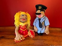 Pair of Melissa & Doug hand puppets; police officer and cheerleader against a red background on a wooden surface.