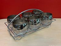 Set of six vintage roly poly glasses with silver fade band and white floral etching inside original chrome carrier with handle, front angle.