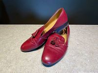 Pair of red leather loafers with tassels on a neutral tabletop, showing toe and vamp details.