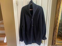 Full view of oversized navy knit cardigan hanging on hanger showing front buttons, shawl collar, and pockets.