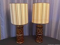 Pair of vintage ceramic table lamps with textured bamboo-style bases and original vertical stripe fabric drum shades in earthy tones, unlit, positioned side by side.