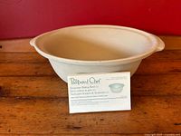 Stoneware baking bowl on wood surface with original care and recipe card placed inside showing product info.