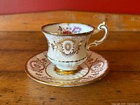 Side angled view of Paragon teacup and saucer set showing gold filigree on the ribbed teacup body and scalloped gold rim on saucer.