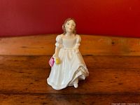 Front view of young girl figurine in white dress holding pink basket and yellow flower on wooden surface against red background