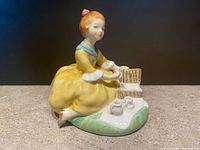 Front and side view showing detailed painting of young girl in yellow dress with picnic basket and tea set on grass base.