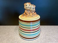 Front view of the closed cookie jar displaying the tiger cub lid and the multicolored striped body.