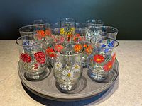 Front view of all 12 glasses arranged on a tray showing colorful floral prints and clear glass shape.