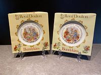 Two Royal Doulton Bunnykins commemorative plates in original boxes showing front of boxes with plate image and decorative elements.