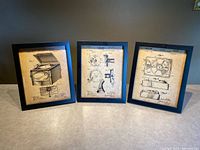 Three sepia-tone framed patent print illustrations shown standing side-by-side. Each framed print depicts a different vintage phonograph or record player patent drawing with black frames and aged parchment backgrounds.