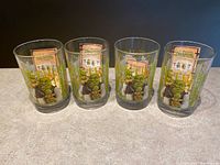 Four clear collectible drinking glasses with colorful Shrek Forever After artwork and original promotional inserts visible inside each glass, arranged in a row