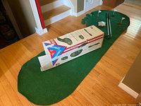 Full view of green putting mat rolled out on floor with original Spalding box on top showing branding and product information.