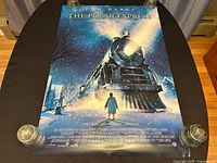 Front side of the Polar Express movie poster laid flat on a black table, showing full artwork with train and child in snow at night.