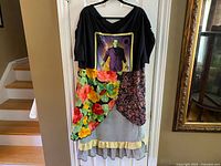Full-length photo of the upcycled dress hanging on hanger showing graphic Frankenstein tee bodice and colorful patchwork skirt with floral prints and ruffles.