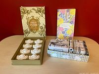 Photo showing two soap gift sets side by side: Avon boxed set with white cherub soaps; Beekman 1802 floral boxed set with wrapped soaps and hand cream.