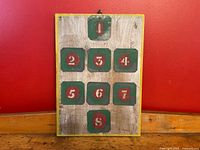 Front view of the vintage industrial number stencils mounted on a wooden crate panel with yellow border and hanging loop.