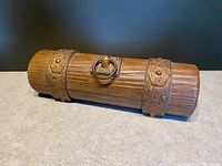 Full view of vintage Avon trinket box shaped like a medieval scroll case, showing faux wood texture and embossed metal bands with lion head ring handle.