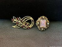 Photo of vintage cocktail ring with iridescent pink/gold stone and gold-tone leaf-shaped brooch with purple rhinestones on black background