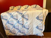 Photo of the quilt spread over a black surface showing the fan pattern in pastel blues and floral prints on white background, scalloped edges visible.