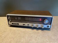 Full front view of vintage Lloyd’s Multiplex stereo clock radio showing woodgrain case, flip clock displaying 4:20, AM/FM tuning dial with stereo indicator light on, and headphone jack.