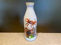 Front view of vintage milk bottle upright on flat surface showing cartoon cow design.