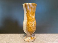 Front view of tall onyx marble vase showing golden and cream swirling pattern and flared rim detail.