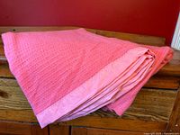 Folded pink textured blanket with satin trim placed on wooden surface, showing blanket thickness and satin edge.