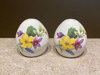 Front view of two egg-shaped salt and pepper shakers showing colorful floral design on white glossy bone china.