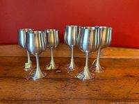 Six vintage Selangor Pewter wine goblets with original tags displayed on wooden surface against red background.