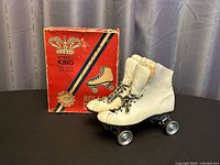 Pair of white outdoor roller skates with metal plates next to the original retail box showing front and side views.