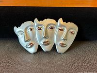 Front view of the vintage triple face brooch showing three stylized abstract faces in brushed silver-tone with polished facial highlights.