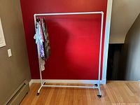 White pipe clothing rack against a red wall, some clothes hanging, showing height and length.