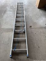 Full view of the collapsed aluminum ladder lying on the ground, showing the length and overall condition.