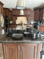 Overview of two sets of matte black stoneware dishes including stacks of plates, bowls, and cups on a kitchen island.