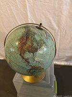 Front view showing North and Central America on rotating globe on brass-colored stand.