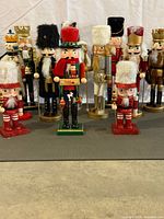 Front view of all eleven painted wooden nutcracker soldier ornaments arranged on grey mat