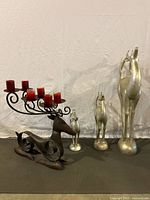 Photo of rustic large steel reindeer candle holder with 8 red candles alongside three stylized silver-tone reindeer figurines of varying heights