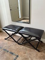 Side view of two benches side by side with faux brown leather seats and black metal X-frame bases in entryway setting.