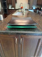 Side view of stacked serving platters: one black ceramic and two green glass platters, showing their shape and relative thickness