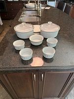 Photo showing two large white Corningware dishes with glass lids and one plastic lid, plus four small ramekins arranged on black countertop