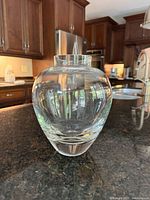Front view of clear lead crystal vase showing rounded body and neck opening on dark stone counter in a kitchen.