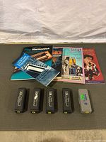 Five closed harmonicas with four black cases and one gray case, laid in a row with instruction booklets behind them on a mat.