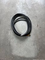 Full view of coiled black hose on concrete floor showing length and condition.