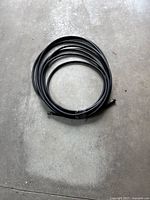 Coiled black hose approximately 50 feet long, laid on concrete floor.