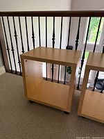 Light wood solid side table with casters on carpet, showing rectangular shape and shelf pegs without shelves